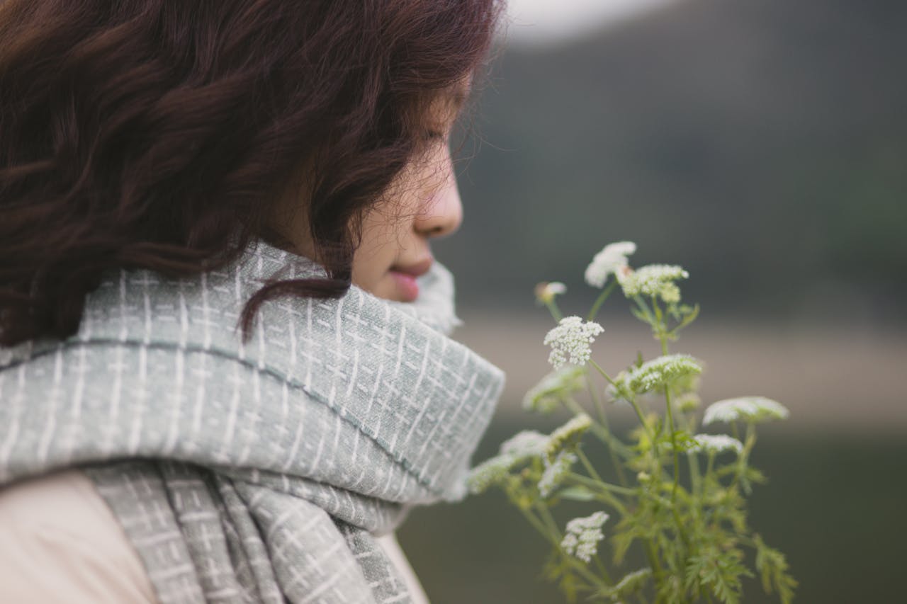 hero-img-02 A contemplative woman in a scarf enjoys wildflowers outdoors.